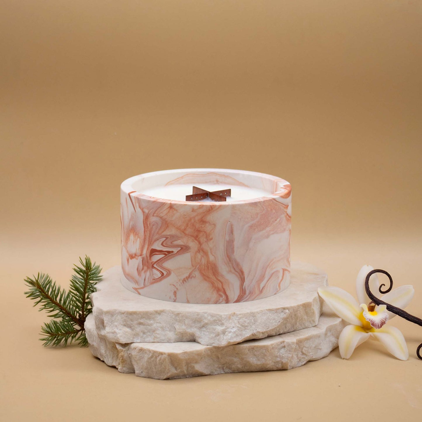Grande bougie ronde artisanale marbrée en terracotta avec une mèche en bois, posée sur une pierre naturelle, accompagnée d'éléments évoquant la vanille boisée, sur un fond beige.